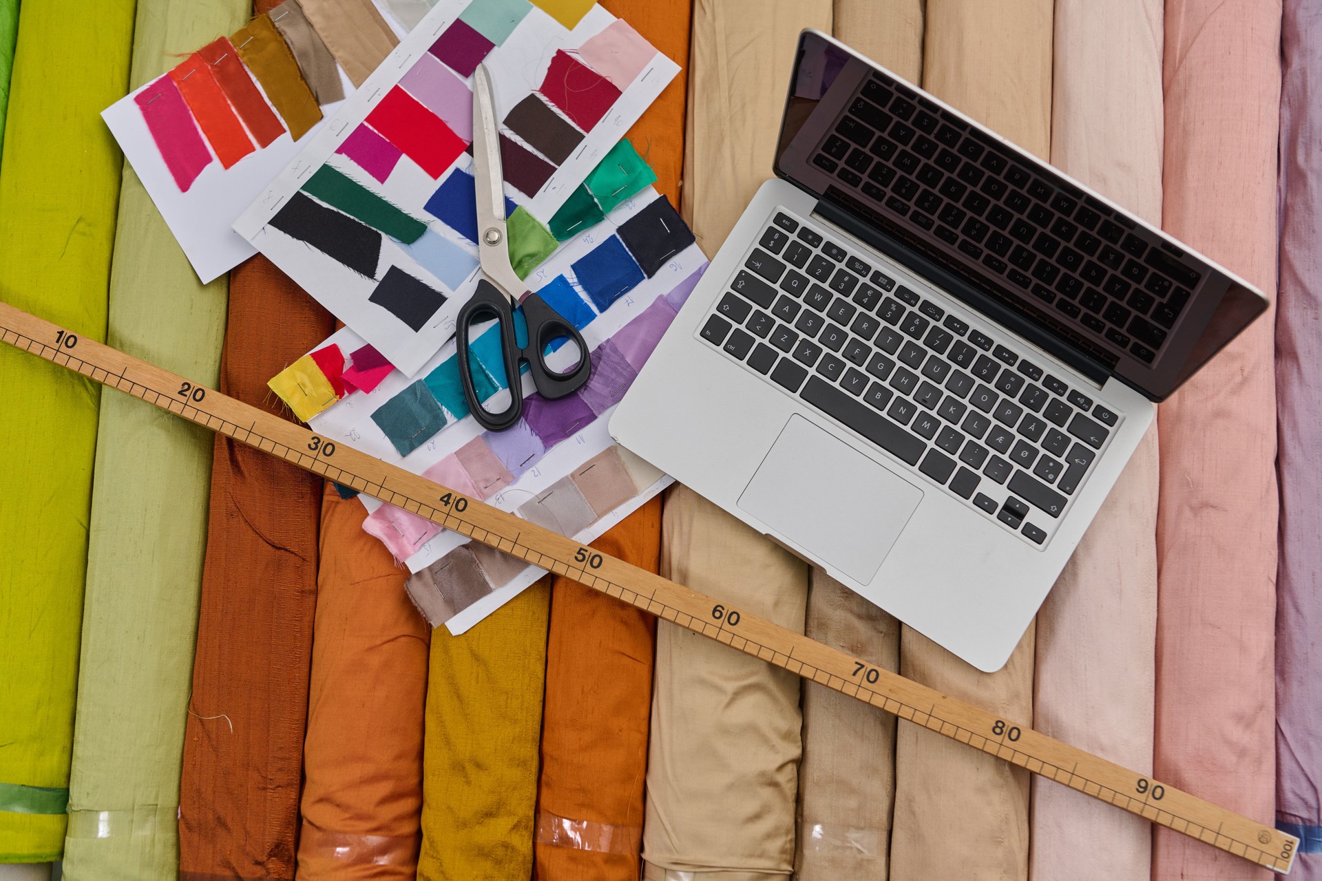 Rouleaux de tissu et ordinateur portable, processus de design, échantillons de couleur, ciseaux et règle sur fond textile, espace de travail créatif, design de mode, prise de vue en studio.