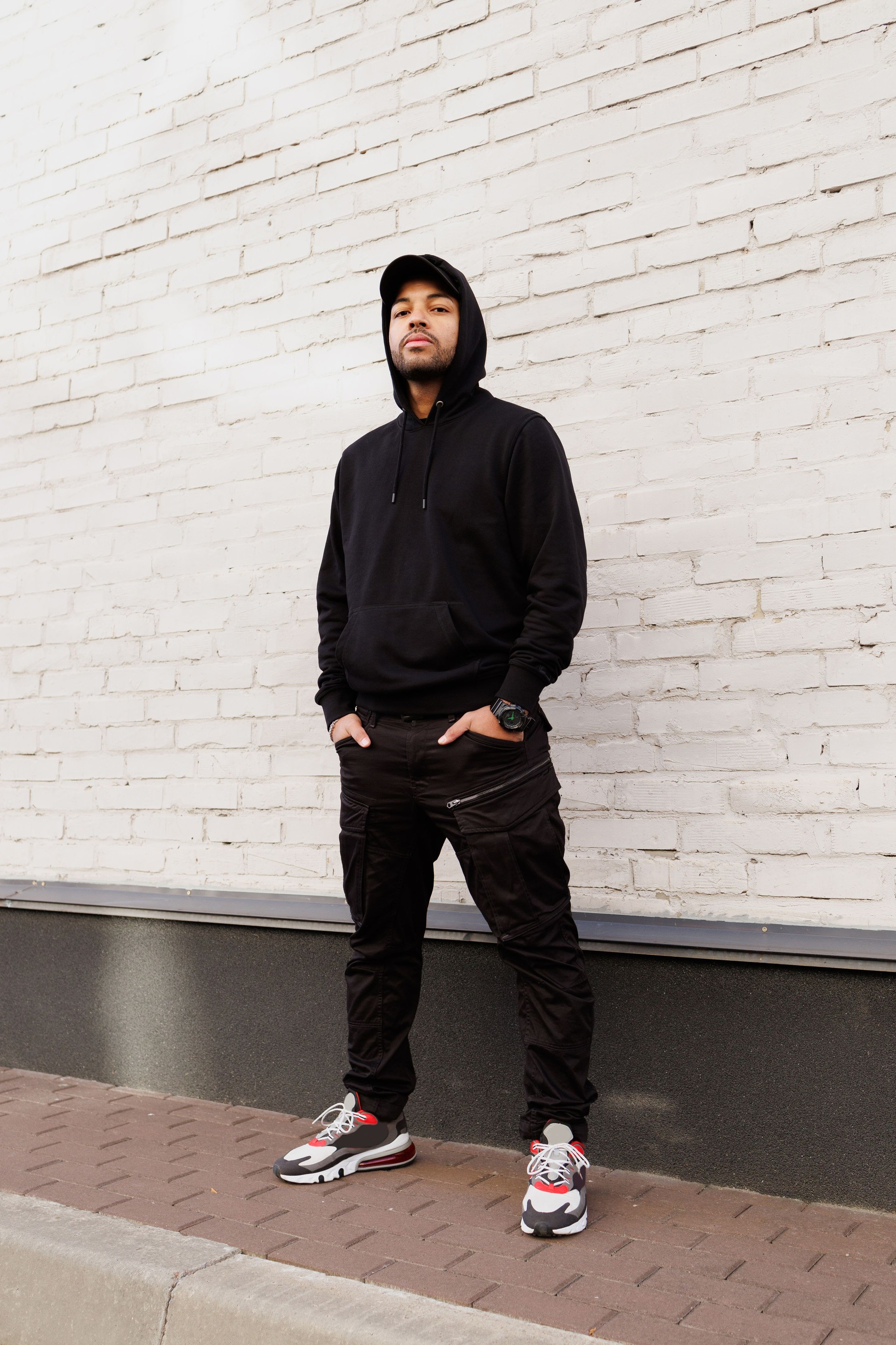 Homme afro-américain confiant en sweat à capuche regardant la caméra près du mur de briques dans la rue