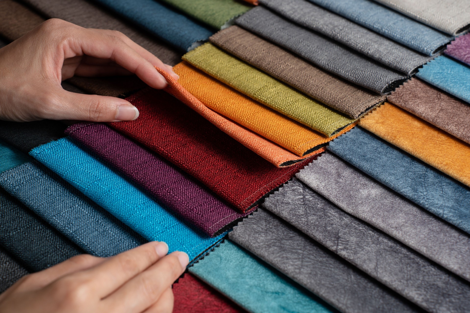 Asian woman's hand touching fabric swatches to assess quality and choose from different colors.