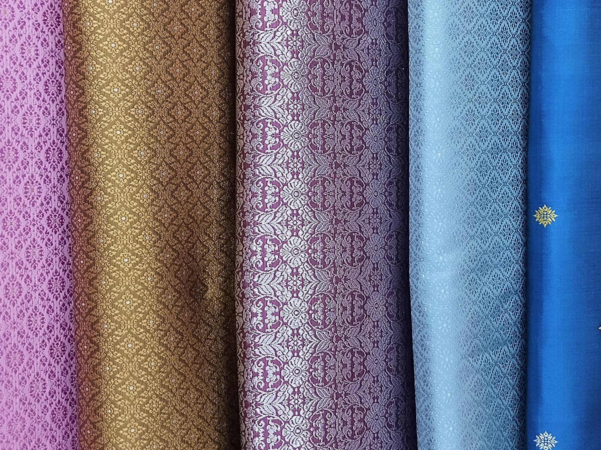 A stunning collection of exquisite silk cloth, meticulously crafted with detailed patterns, reflecting light beautifully across their diverse and rich hues.