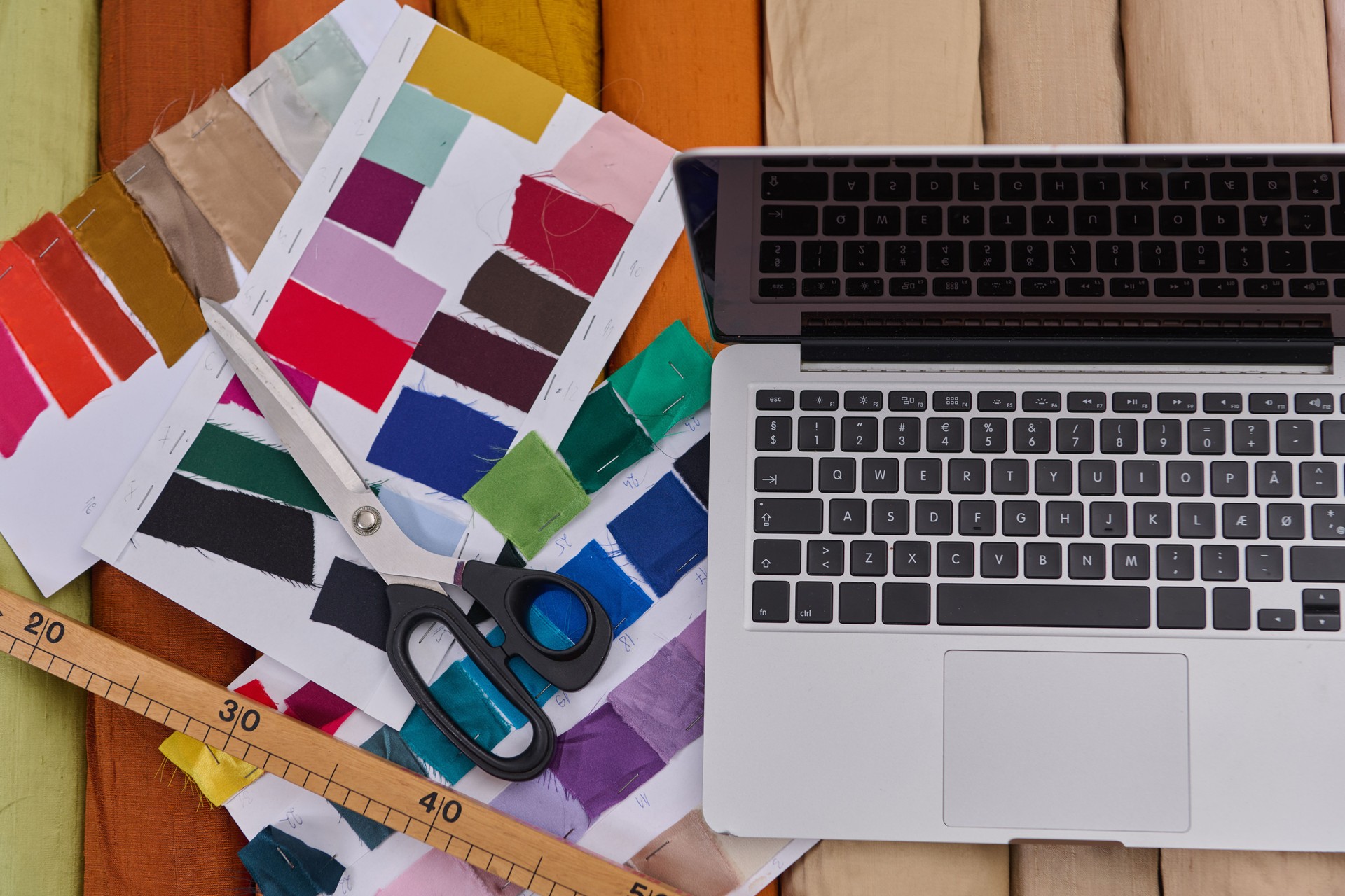 Espace de travail de créateur de mode avec ordinateur portable, échantillons de tissu, ciseaux et règle, vue de dessus. Concept de studio de design, processus créatif, industrie textile, maquette de boutique en ligne.